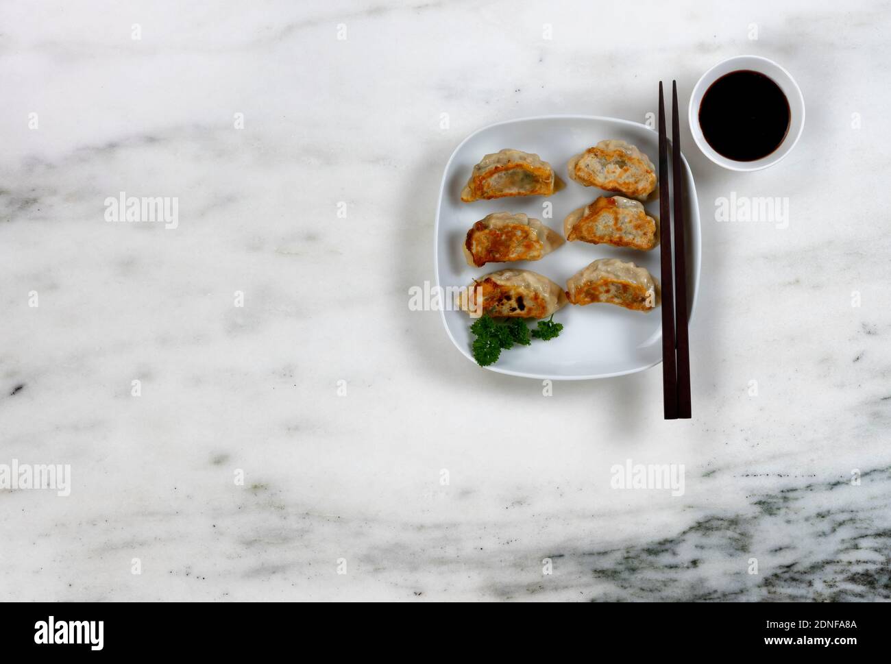 Plate filled with freshly fried Chinese dumplings and dipping sauce on marble top table Stock Photo
