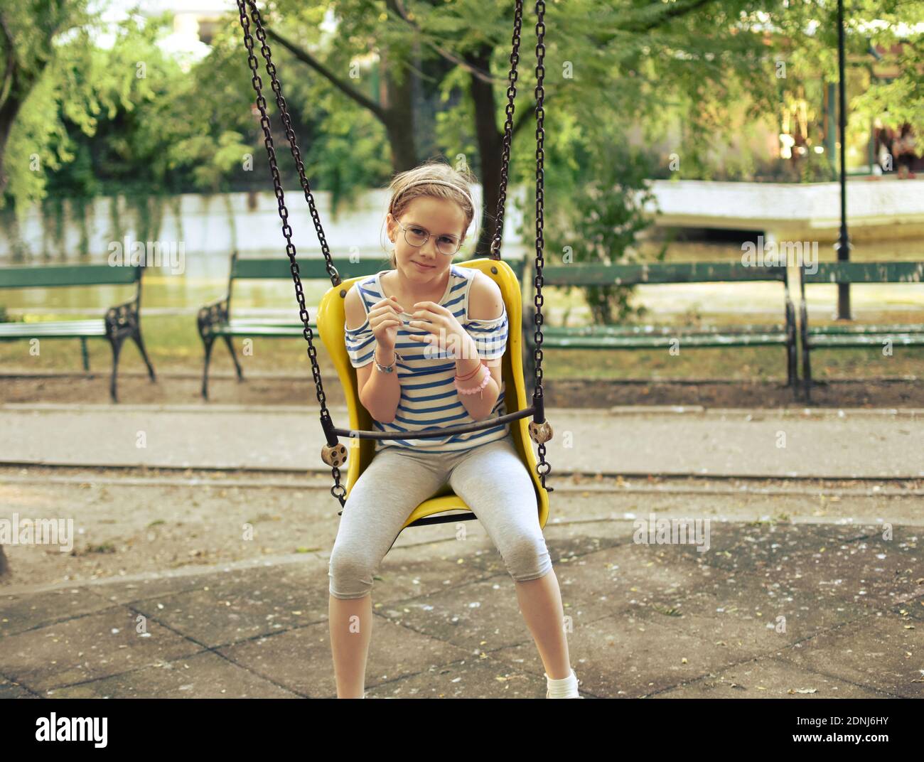 White Caucasian child (girl) swinging at the playground in the park. Stock Photo