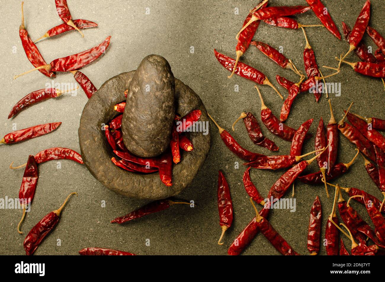Indian stone Mortar and Pestle Set with Dried Red Chili in Mortar.Dried Red Chilis spread all over. Studio Shot Stock Photo