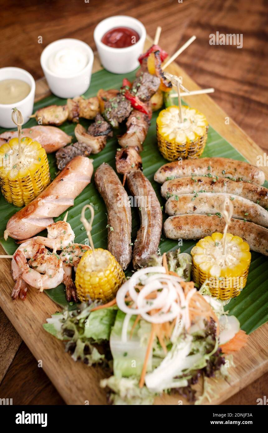 organic mixed grill barbecue meat platter rustic set meal with sausages, skewers, side dishes and sauces Stock Photo