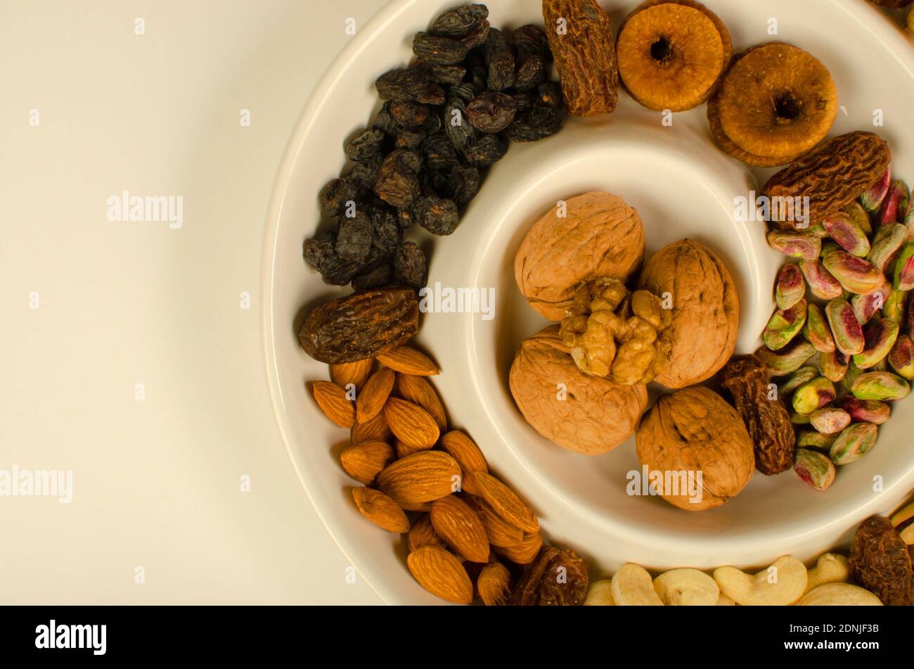 Dried Fruit Almonds, Green Pistachio, Walnut with Shell, Walnut Kernel, dried Fig and dates in white plate . Top angle. Studio Shot Stock Photo