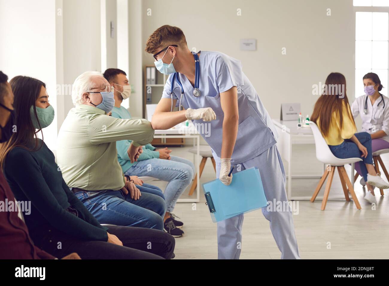 Man doctor in medical protective face mask bumping elbows with mature senior man patient before vaccination Stock Photo