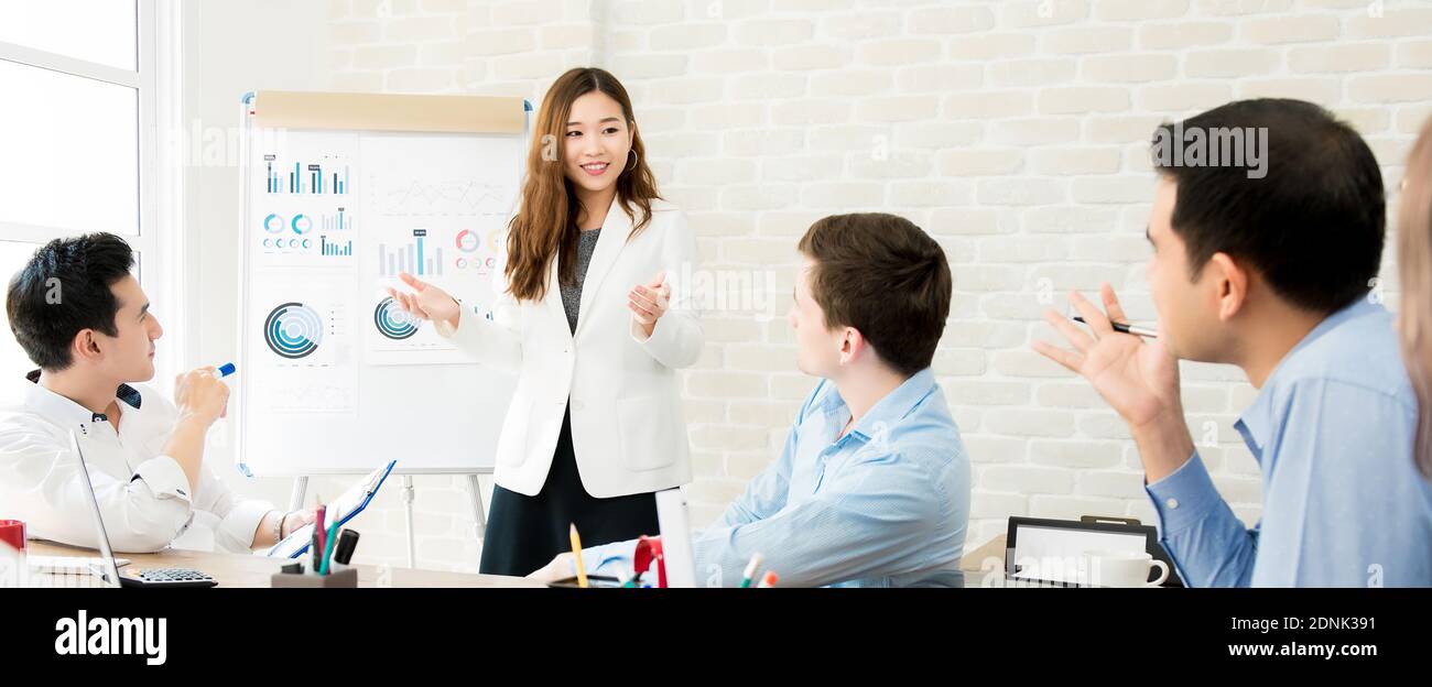 Panoramic banner image of young Asian woman leader presenting financial statistic charts to colleagues in the meeting Stock Photo