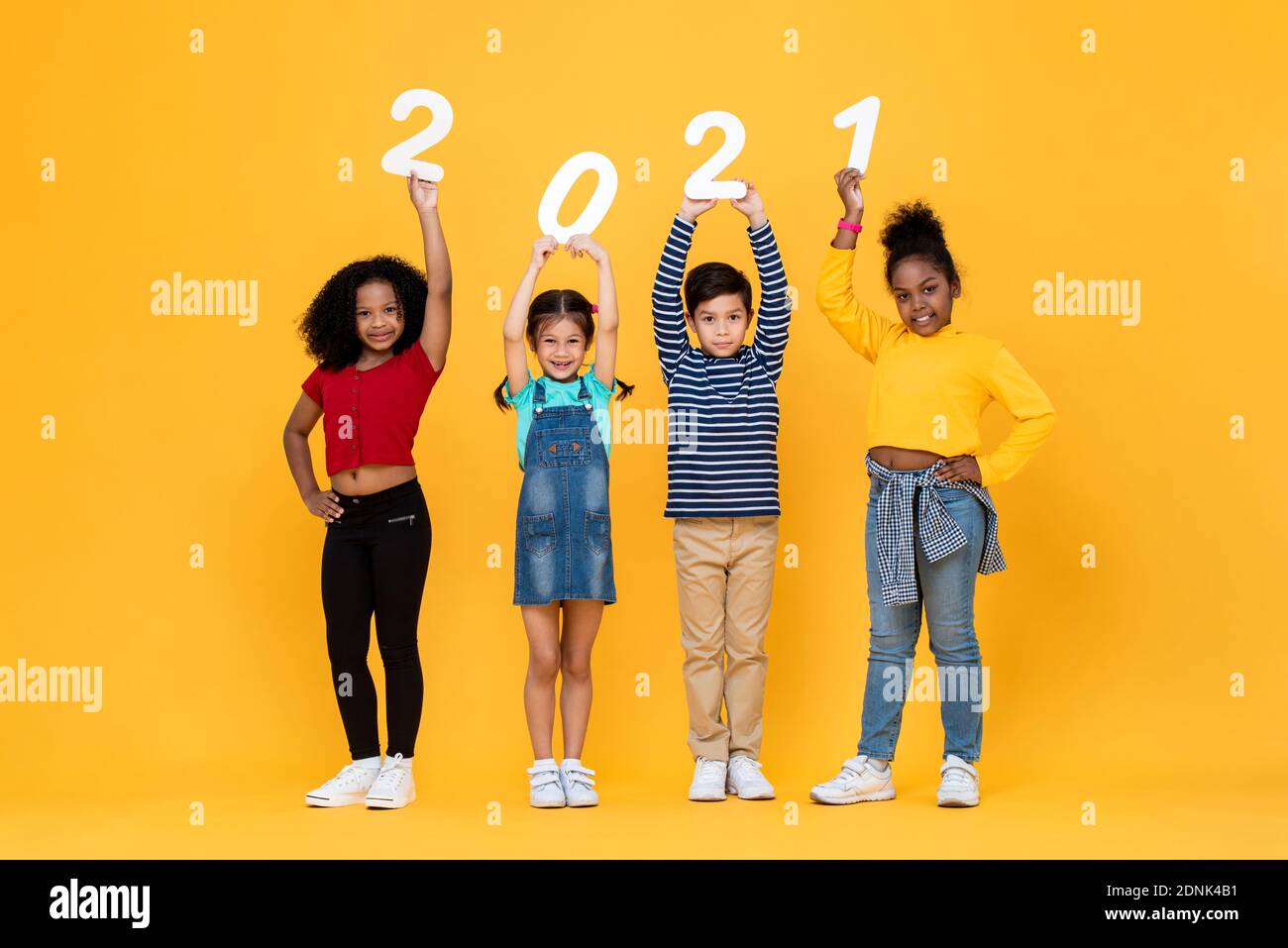 Cute mixed race kids smiling and holding 2021 numbers isolated on yellow background for new year concepts Stock Photo