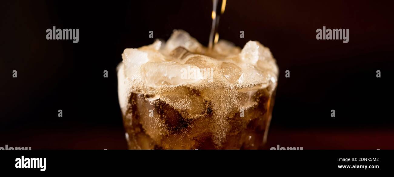 Close up banner of sparkling carbonated cold fresh cola drink being poured into the glass with overflowed frothy bubble on top Stock Photo