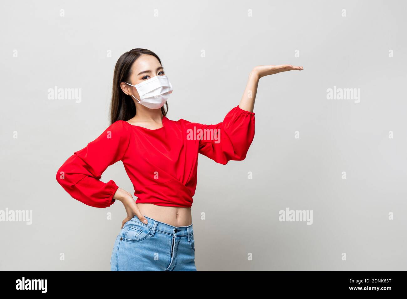 Asian woman wearing medical mask and open hand to empty space aside on light gray studio background Stock Photo