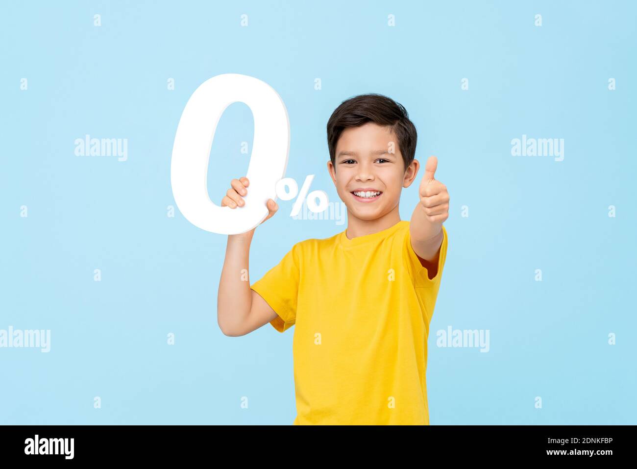 Smiling happy 10 years old mixed race boy holding 0% cutout and giving thumbs up isolated on light blue studio background Stock Photo