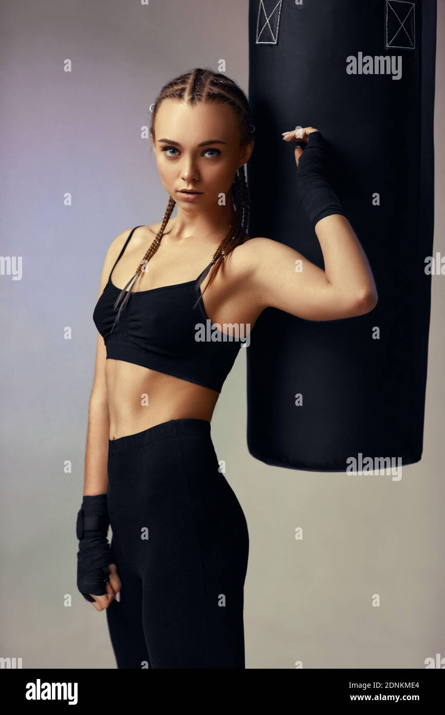 sporty brunette woman in sportswear with boxing bandages near bag on gray background Stock Photo