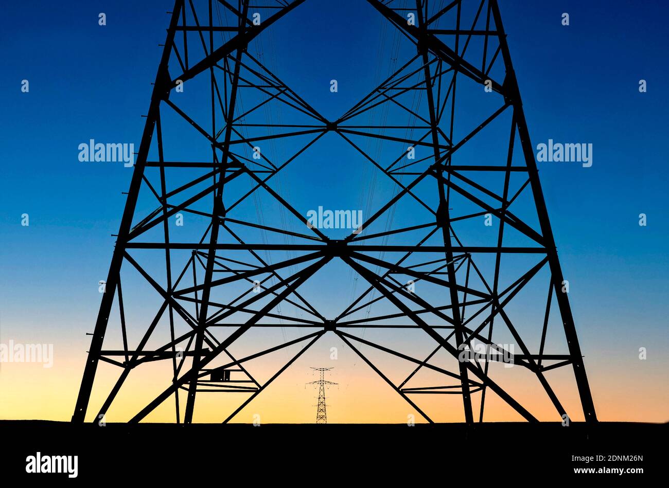 Power transmission tower silhouetted against a vibrant sunset sky with ...