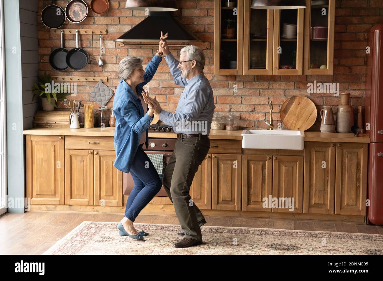 Energetic middle aged family couple dancing in kitchen. Stock Photo
