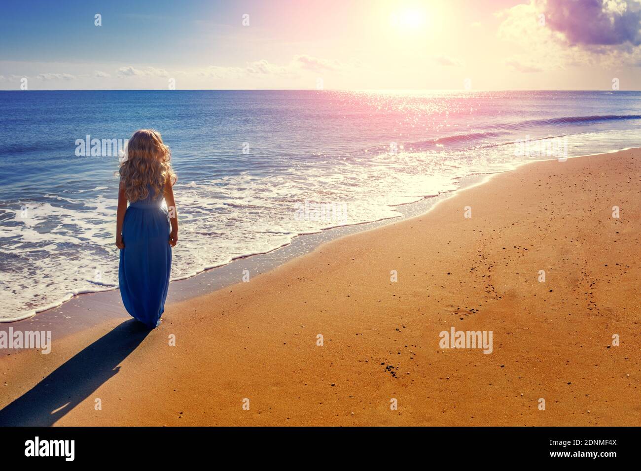 Seascape at sunrise. One woman on the beach. The woman walks along the seashore in a blue long dress Stock Photo