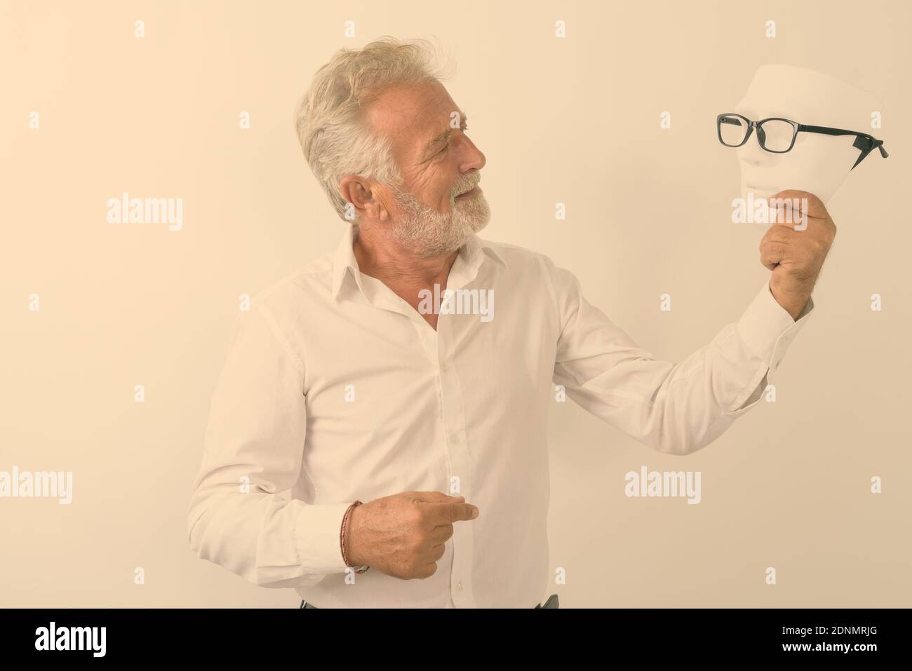 Profile view of happy senior bearded man smiling and looking at white mask with eyeglasses against white background Stock Photo