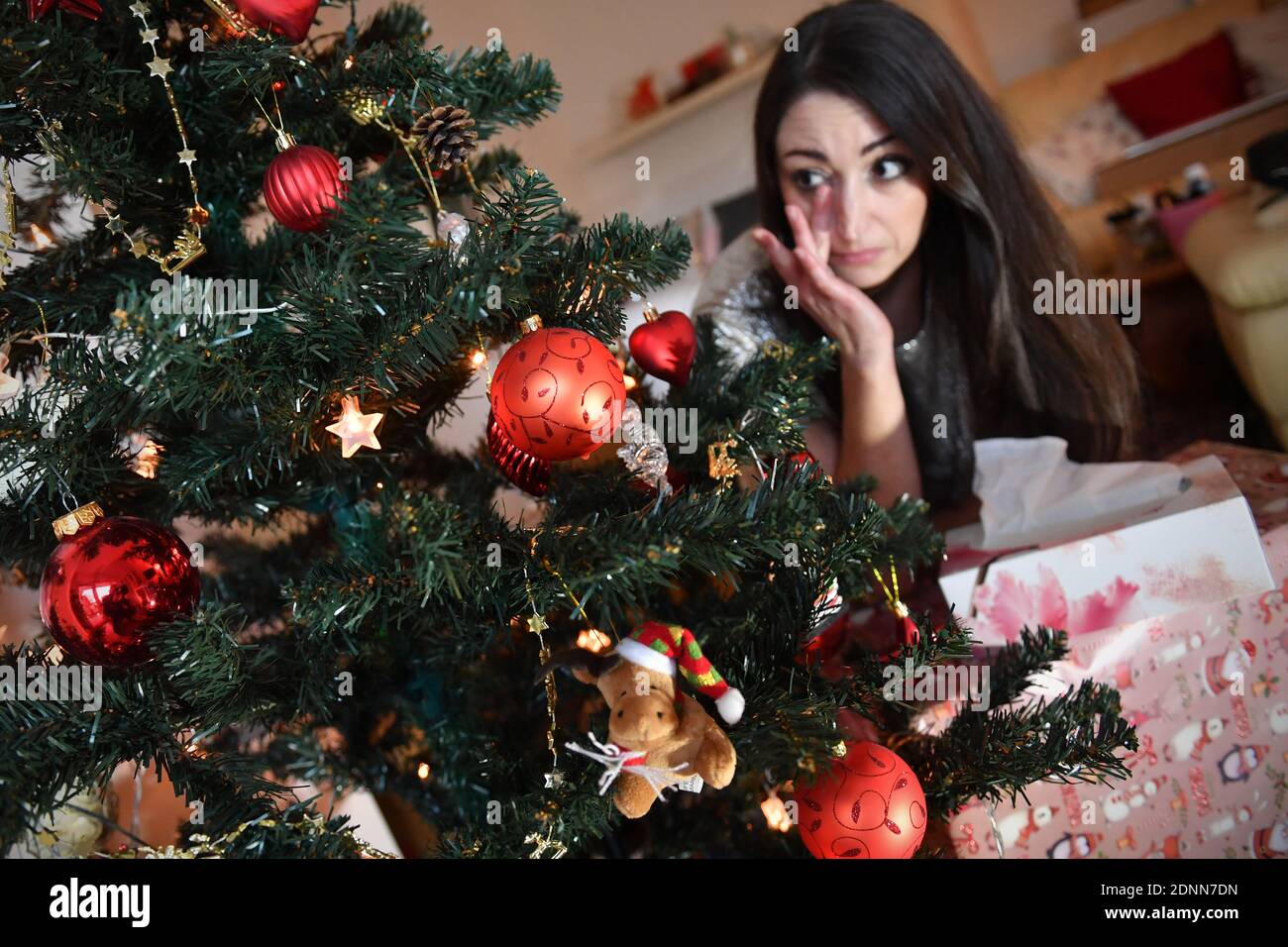 Munich, Deutschland. 17th Dec, 2020. Topic picture Lonely Weihafterten 2020 in the coronavirus pandemic. A young woman with face mask, mask sits alone behind her Weihaftertsbaum on Christmas Eve and is sad, wipes tears from her eyes, weeps, weep, pandemic, lockdown, shutdown, incidence value. MODEL RELEASED! | usage worldwide Credit: dpa/Alamy Live News Stock Photo
