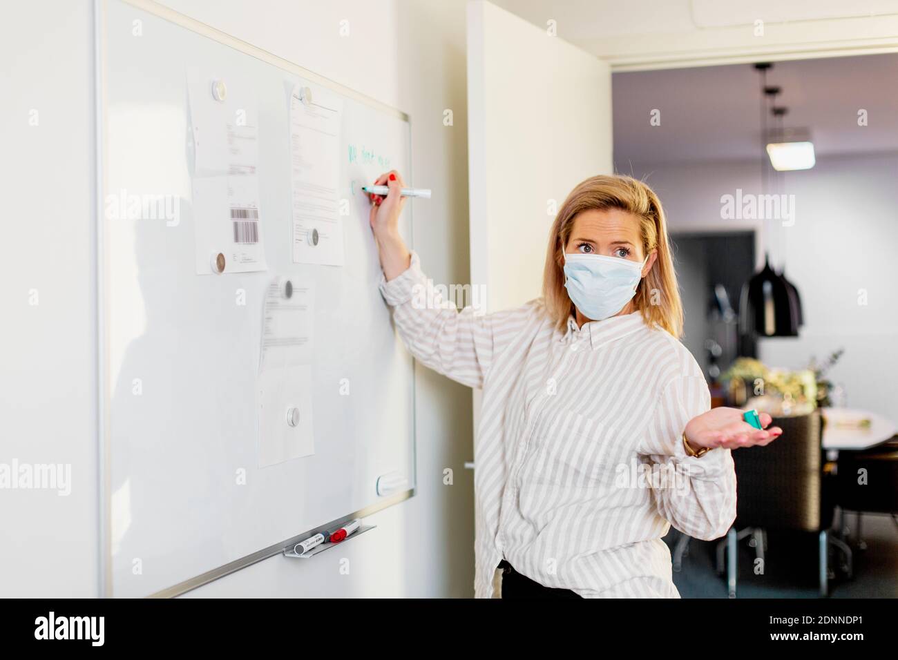 Woman wearing protective face mask writing on whiteboard Stock Photo