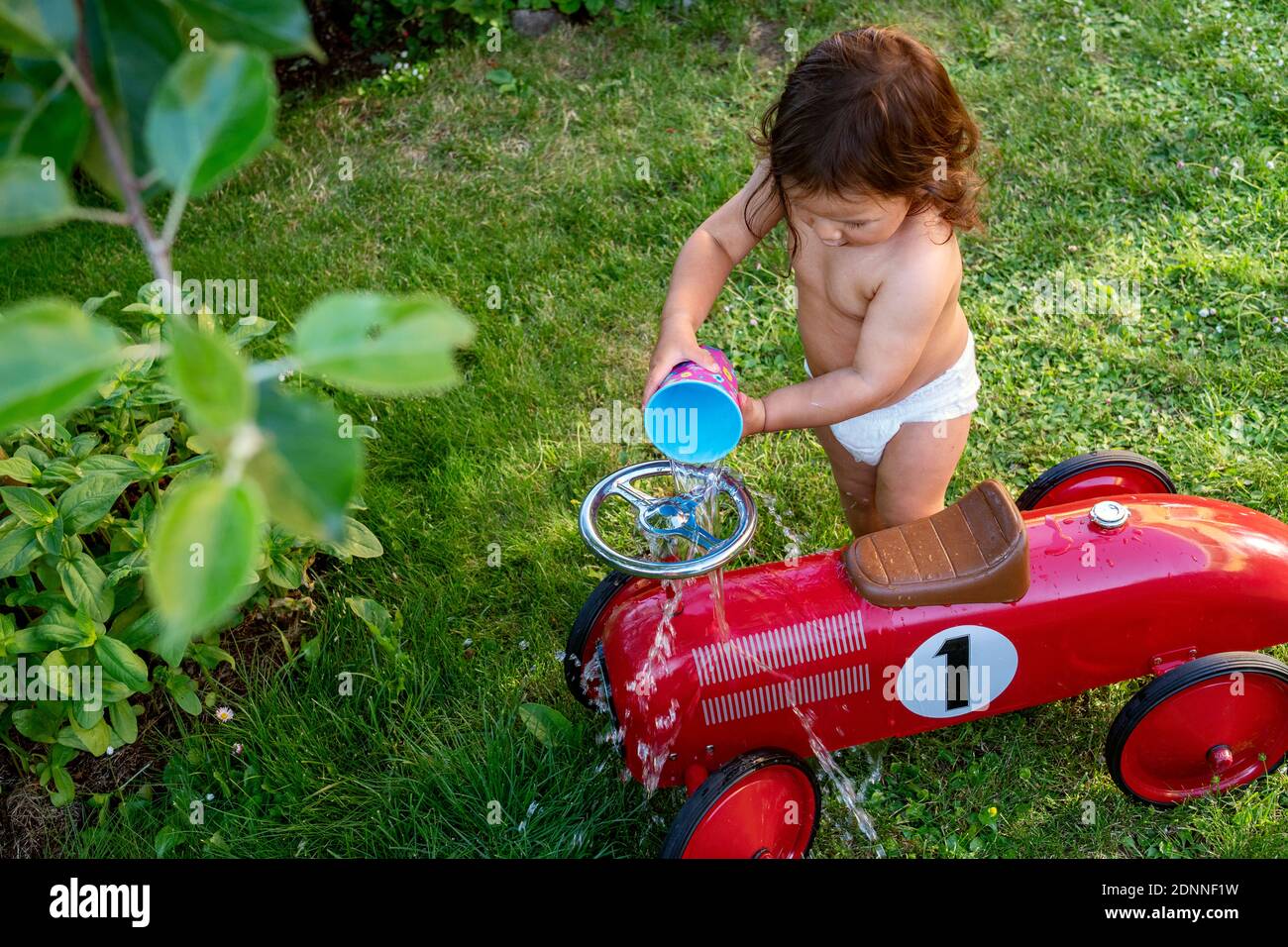 Toddler girl pouring water over ride-on car Stock Photo