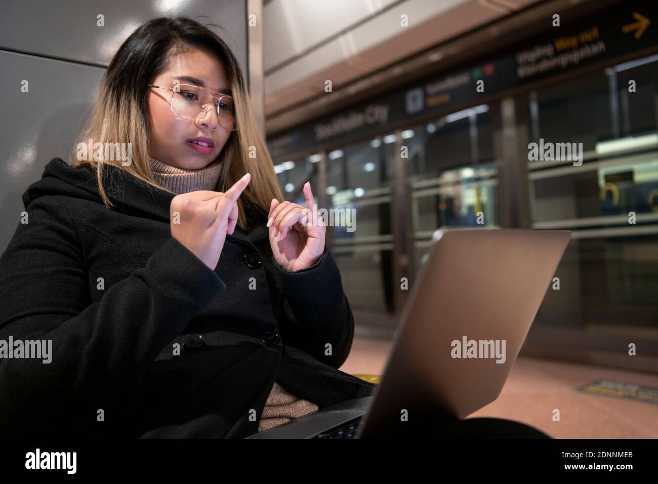 Woman at train station using laptop Stock Photo
