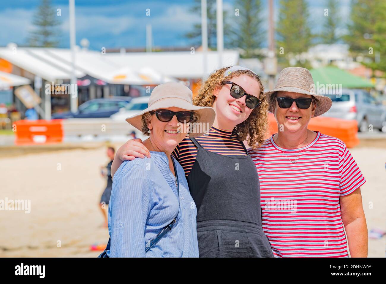 https://c8.alamy.com/comp/2DNNW0Y/two-middle-aged-women-wearing-hats-and-sunglasses-stand-with-a-teenaged-girl-with-curly-hair-in-the-warm-australian-sun-beachside-at-forster-aust-2DNNW0Y.jpg