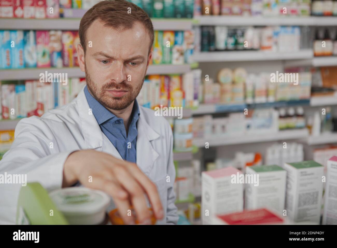 Close up of a mature male pharmacist looking concentrated, organizing medical products on shelves, copy space Stock Photo