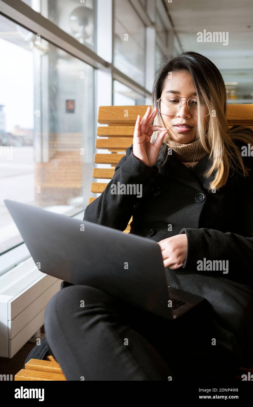 Woman at train station using laptop Stock Photo