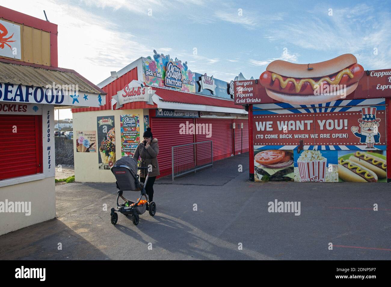 GREAT BRITAIN / Wales /Coney Beach Porthcawl / Woman with pushchair passing the Arcades and amusement park on the seafront . Stock Photo