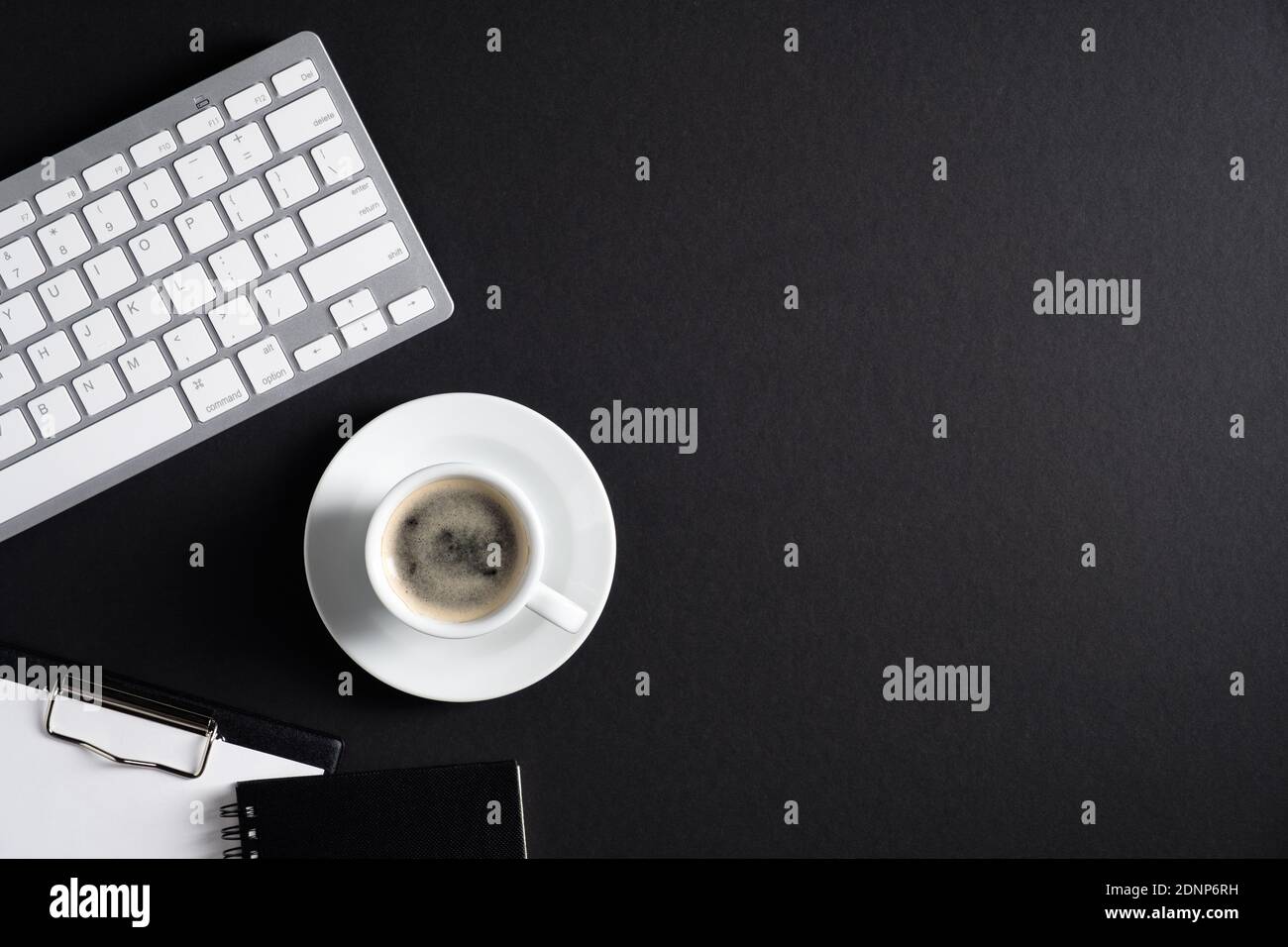 Black office desk table with computer keyboard, cup of coffee, clipboard, notepad. Luxury, minimalist style workspace. Flat lay, top view, copy space. Stock Photo