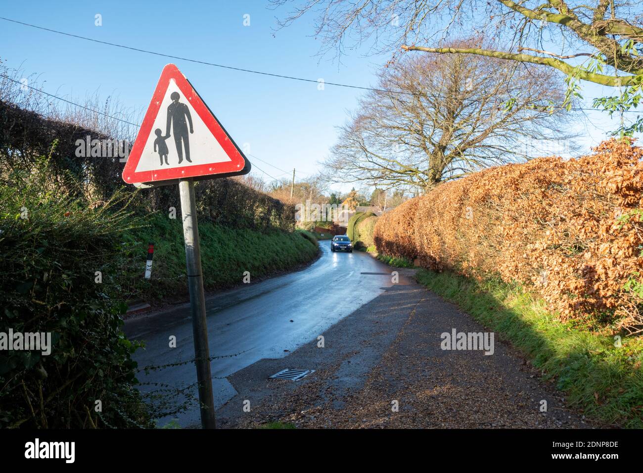 Pedestrians walking red triangle road sign with adult holding hands with a child on a narrow country road near a school, UK Stock Photo