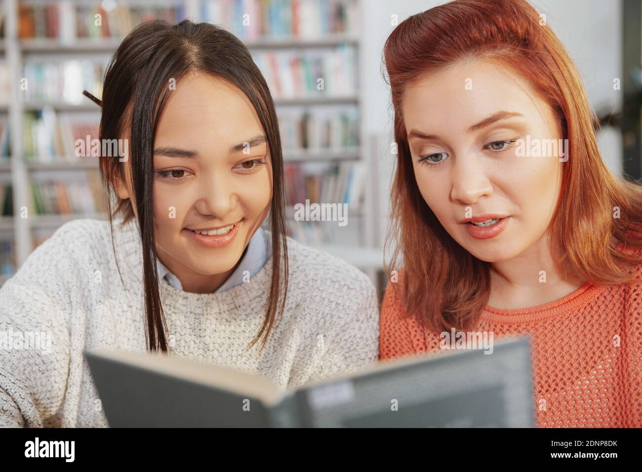 Cropped shot of two young female friends reading a book together at college library. Female students reading Stock Photo