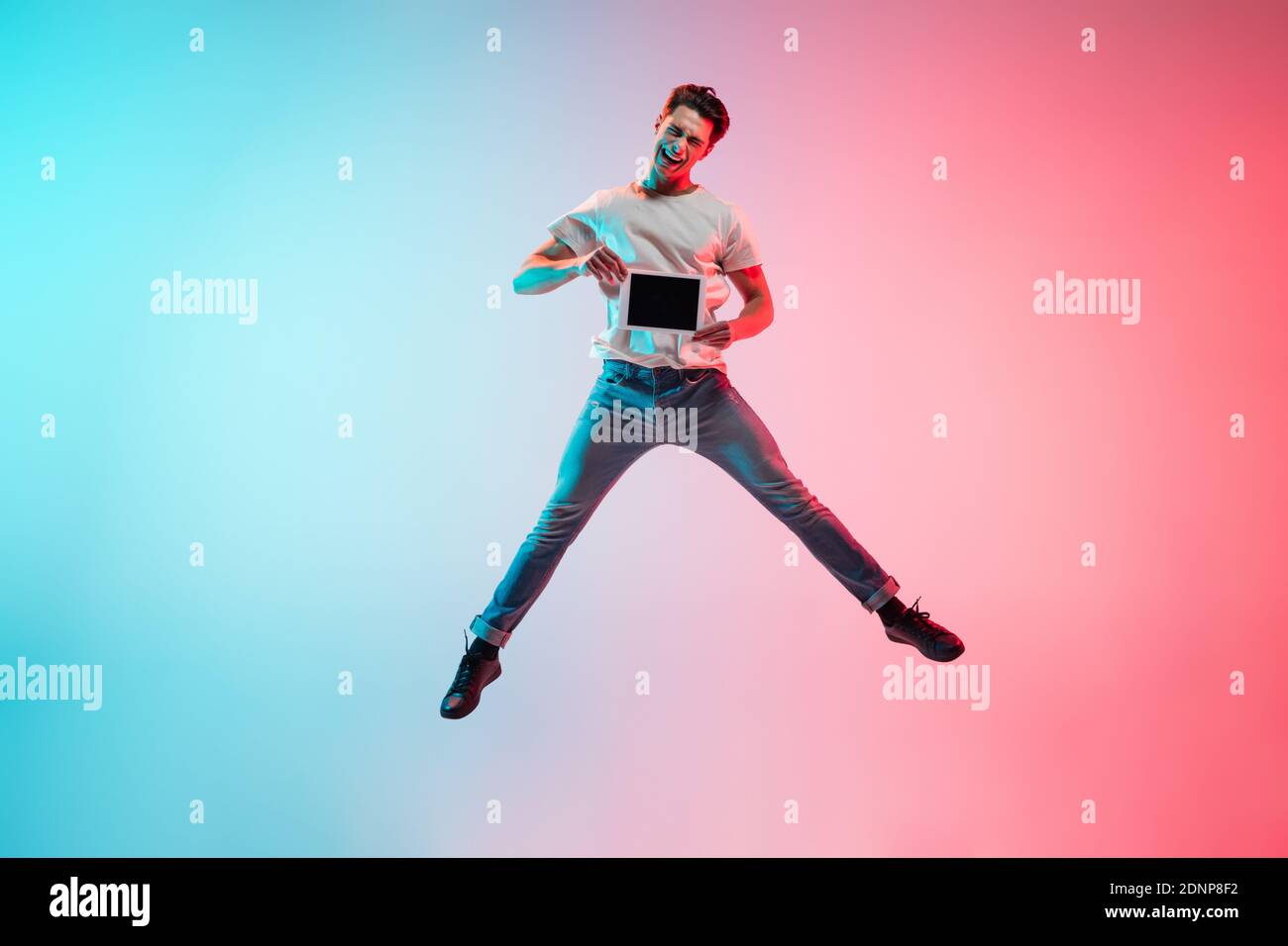 Tablet screen. Young caucasian man's jumping on gradient bluepink