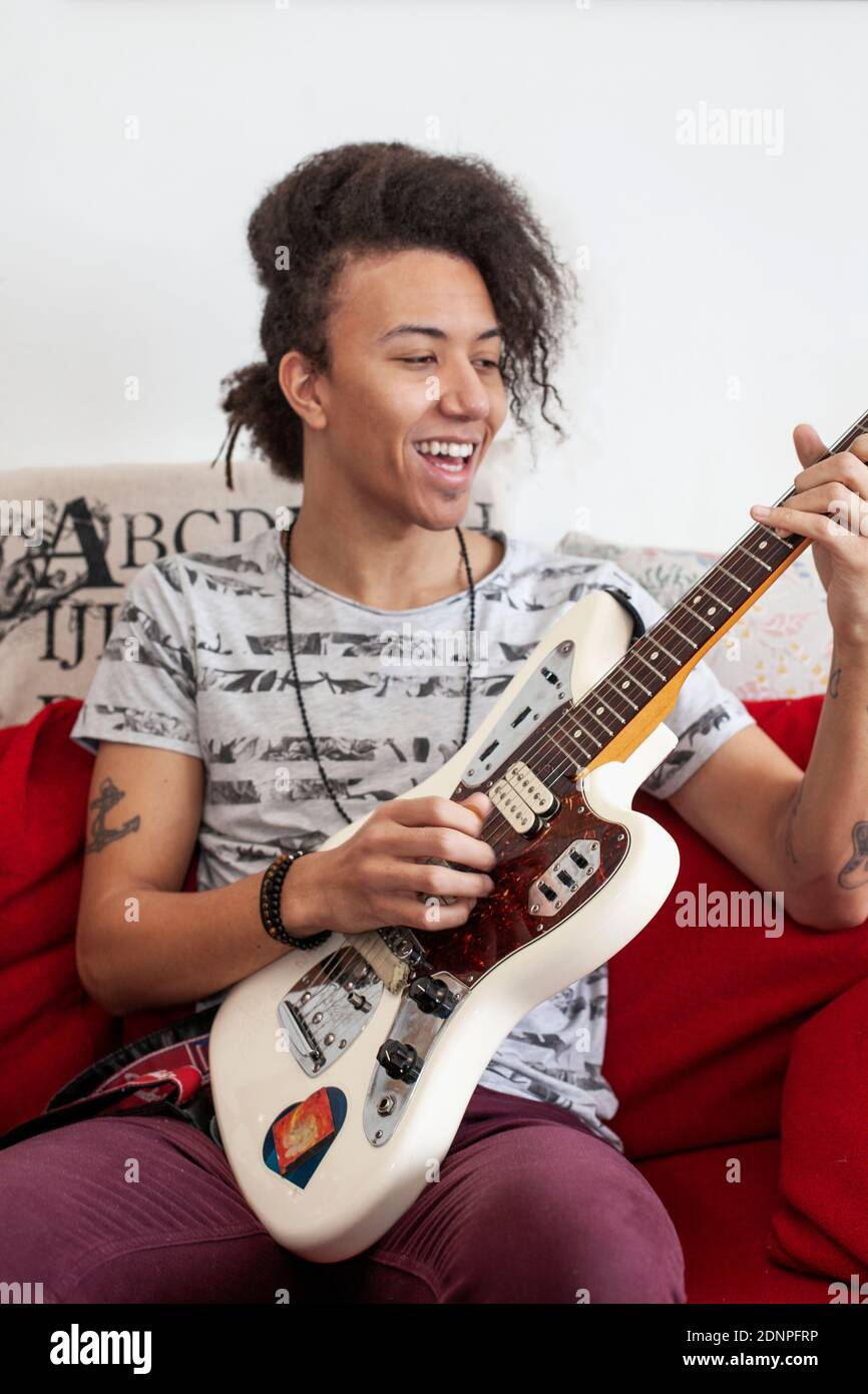 Young man playing guitar on sofa Stock Photo