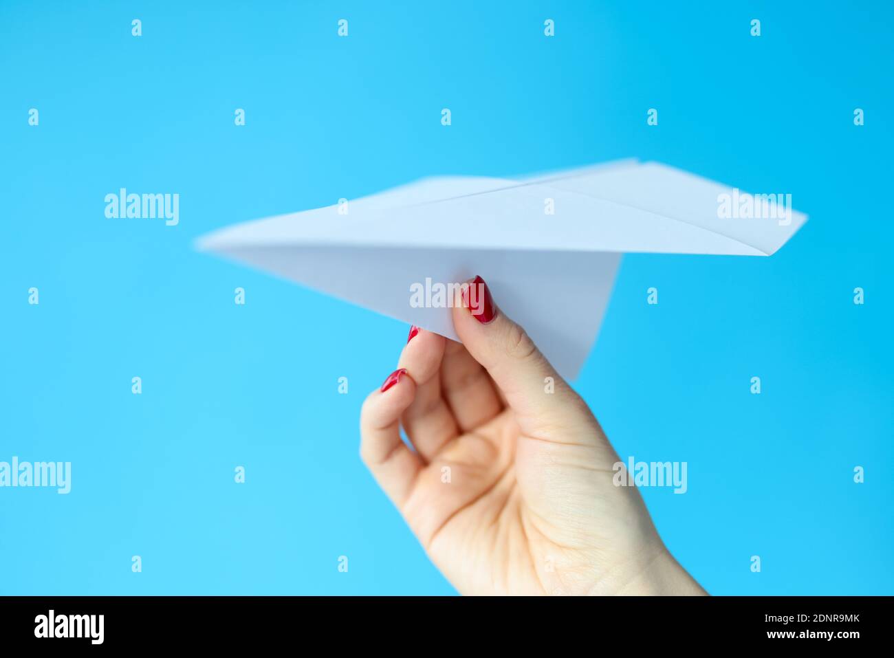 Female hand holding paper plane on blue background Stock Photo