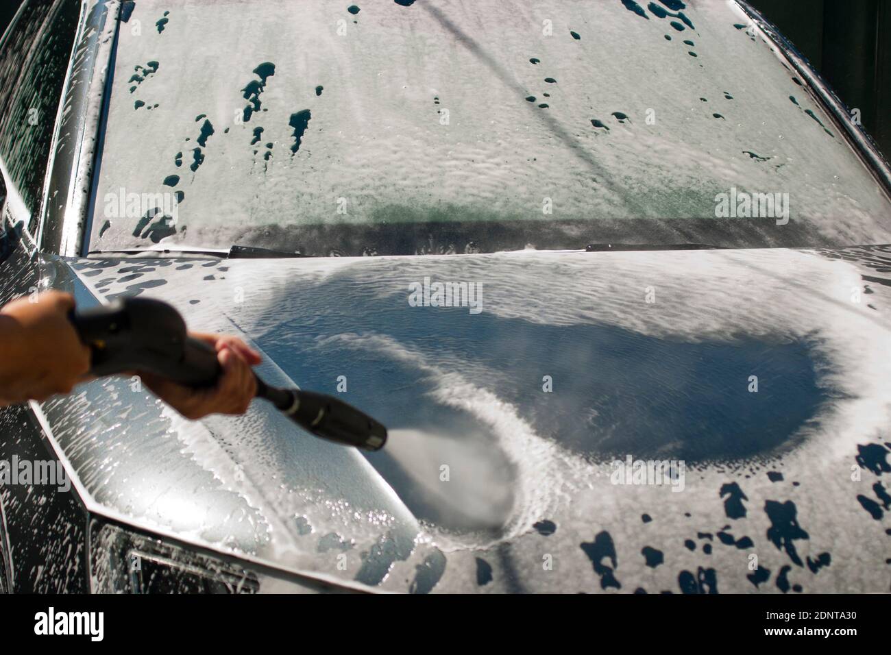 Car washing with high pressure water jet. Water and foam under pressure flies toward the car body. Close-up view Stock Photo