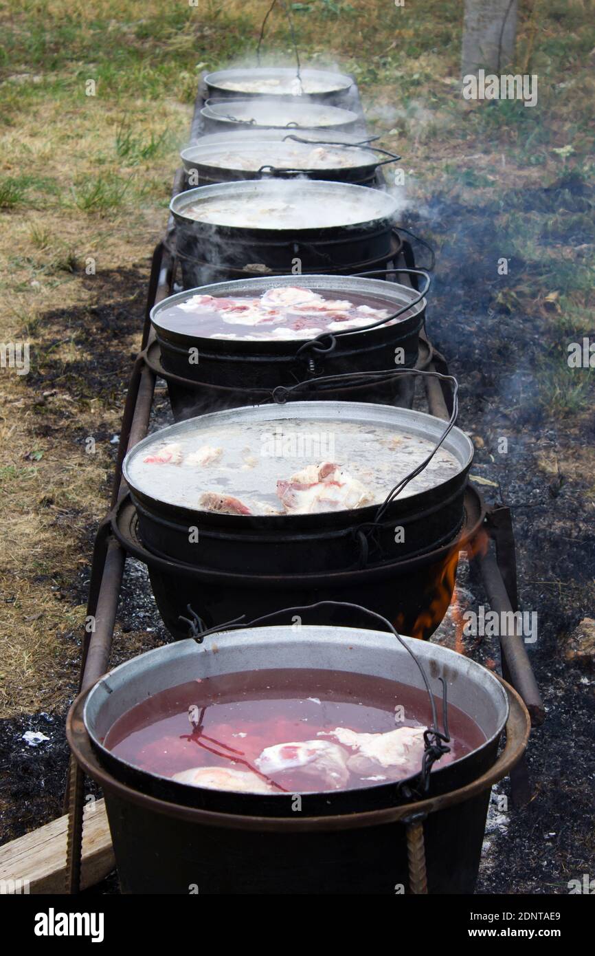 Shurpa is preparing in a cauldron at the stake. Several large cauldrons, lined up with ingredients for shurpa, boil over a bonfire Stock Photo