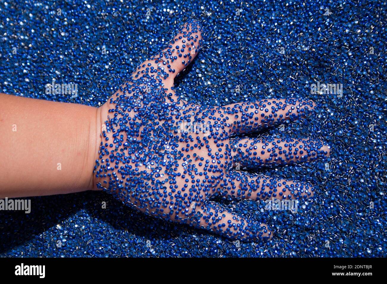 Child's hand in blue rhinestones. A lot of blue glue rhinestones and the kids hand Stock Photo