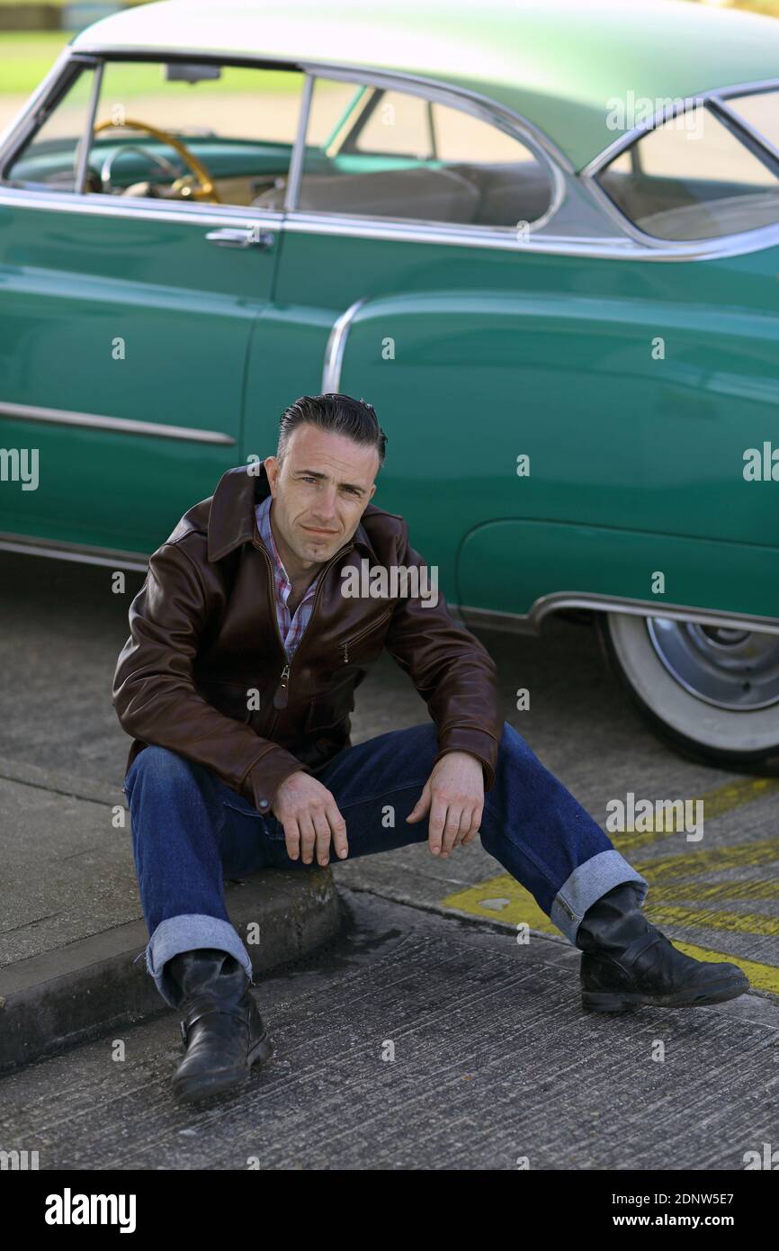 Stylish man wearing leatherjacket sitting in front of vintage cadillac Stock Photo