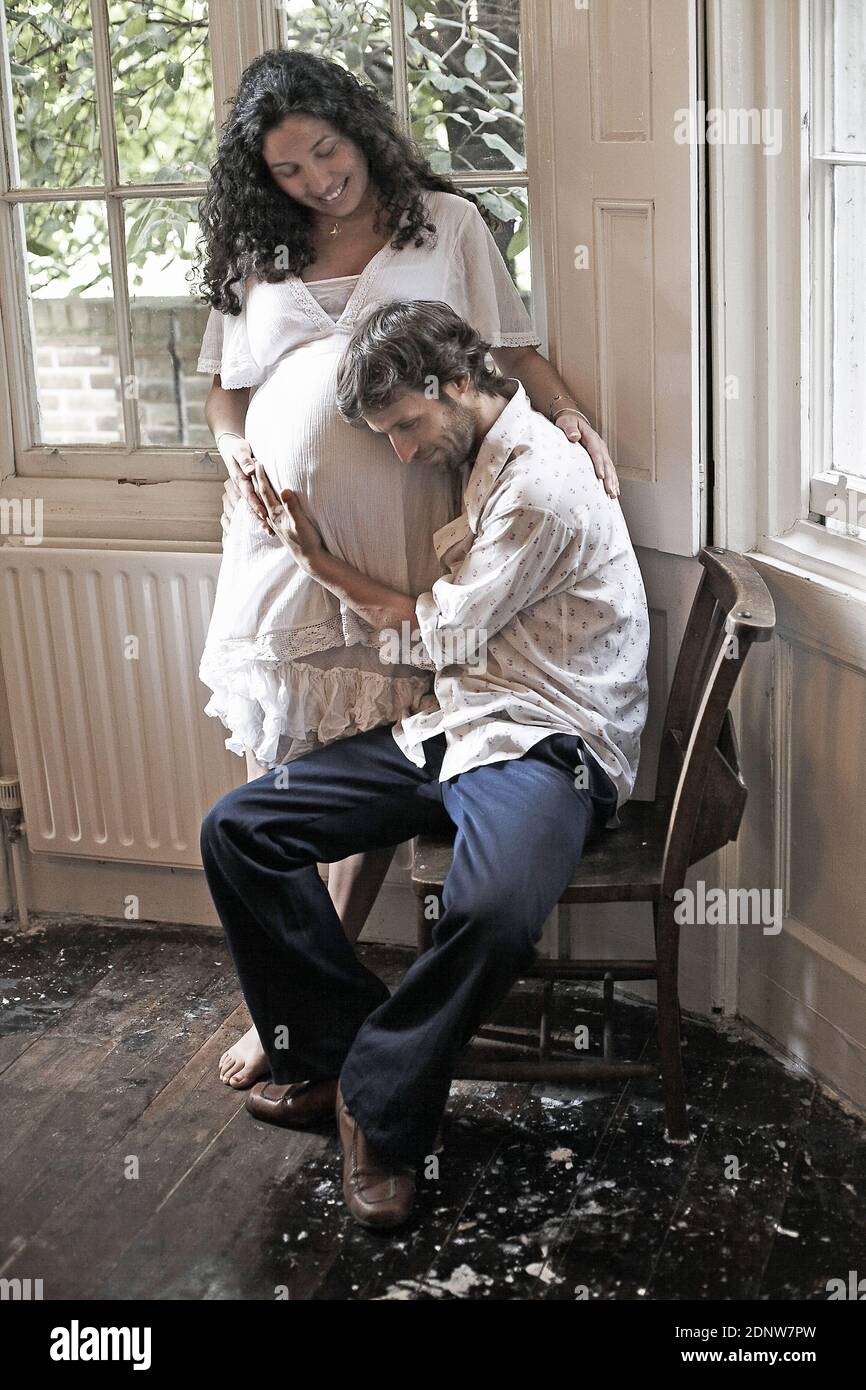 Happy husband listening to baby moving inside his 9 month pregnant wife