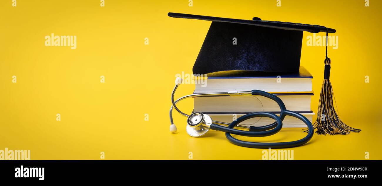 medical education - college graduation cap with stethoscope and books on yellow background with copy space Stock Photo