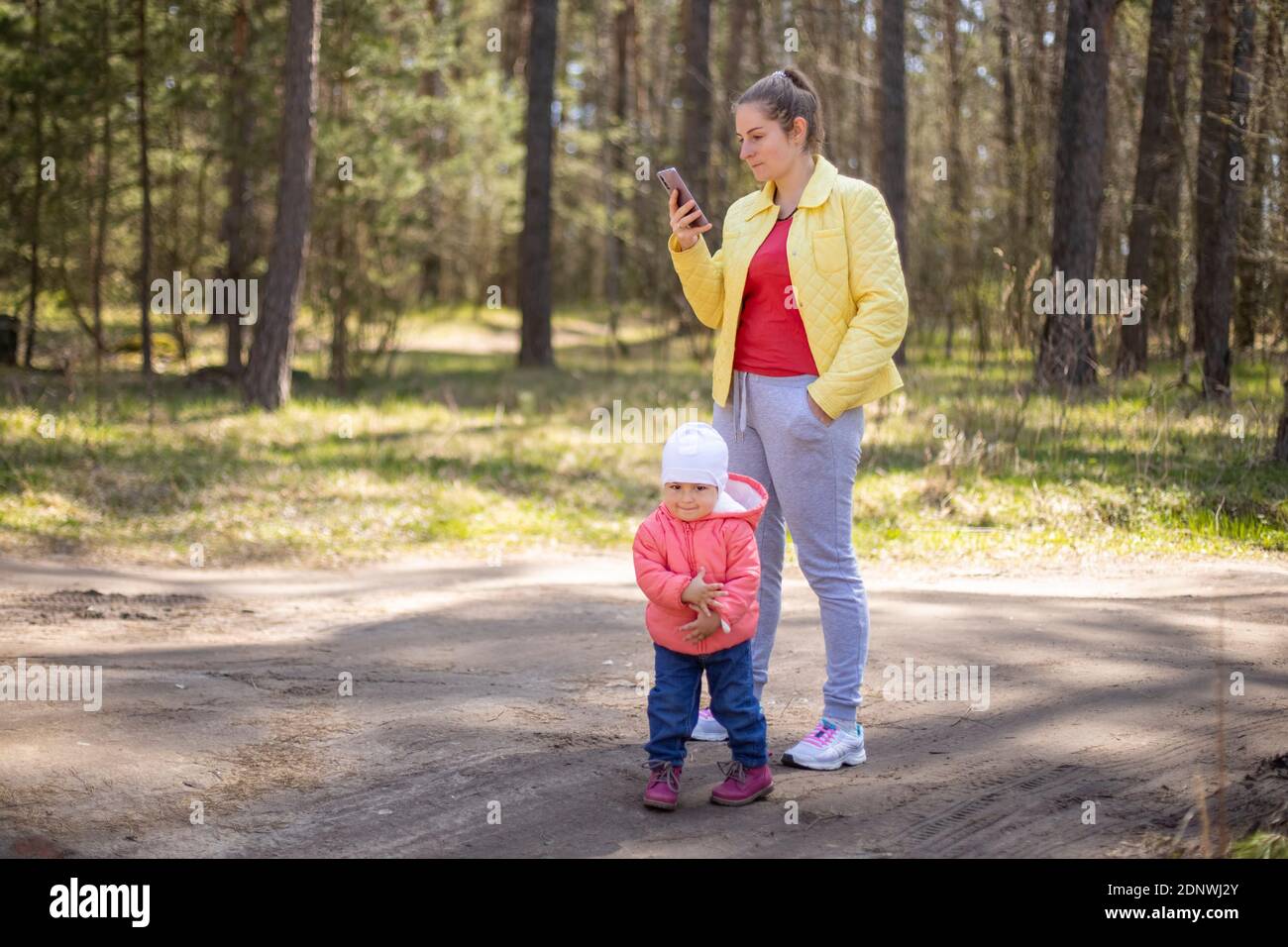 young woman with a baby toddler talking on a mobile phone emotionally in a forest outside the city 4g Stock Photo