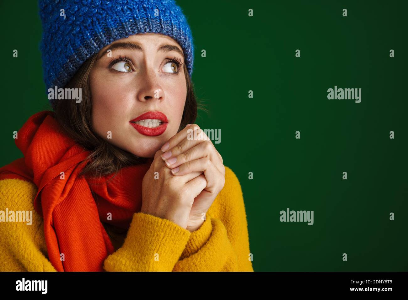 Beautiful unhappy girl in warm hat and scarf posing and trembling isolated over green background Stock Photo