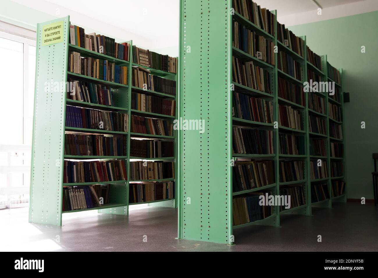 Shelves filled with books in a rural library against the background of a window. Stock Photo