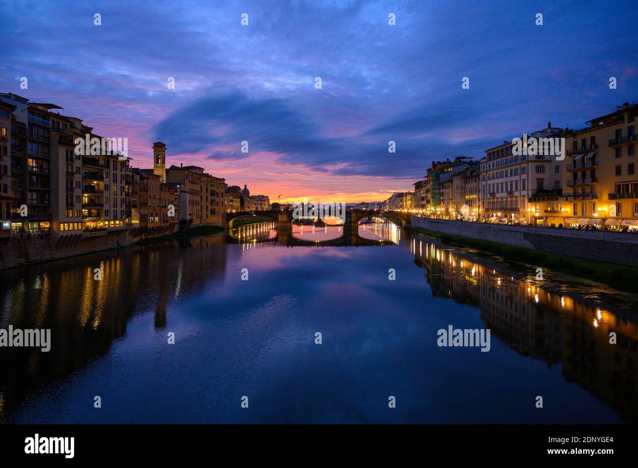 Illuminated Buildings By River Against Sky At Sunset Stock Photo