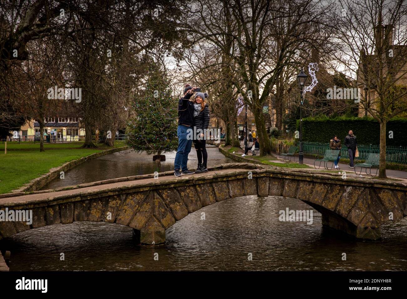 UK, Gloucestershire, Bourton on the Water, couple on bridge taking selfie with Christmas tree in River Windrush Stock Photo