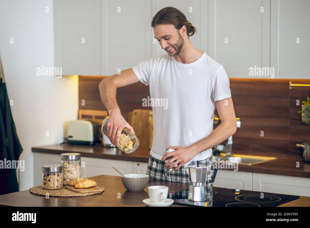Young man in homewear pouring cereal to the bowl Stock Photo