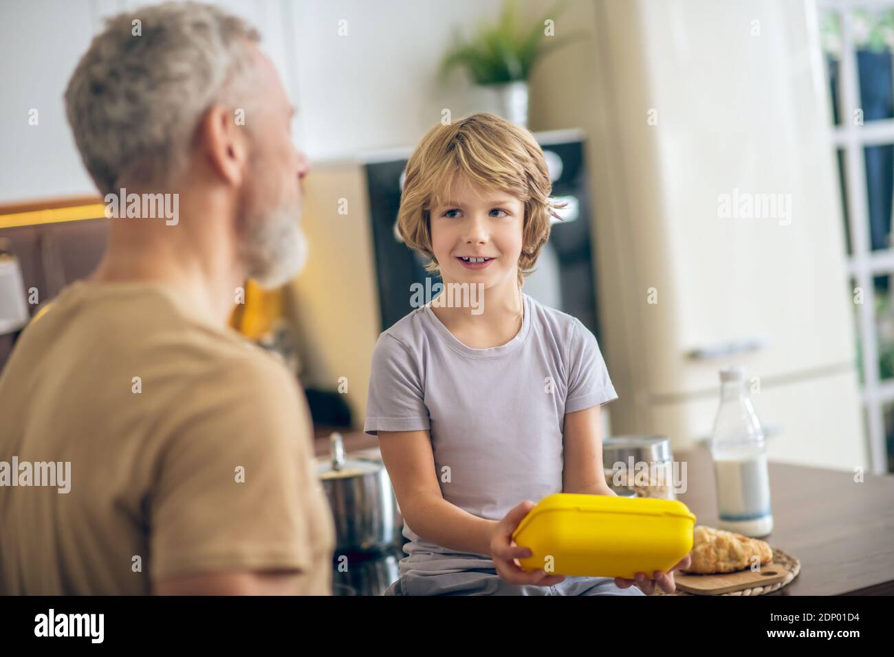 Grey-haired man in beige tshirt and his son in the kitchen at home Stock Photo