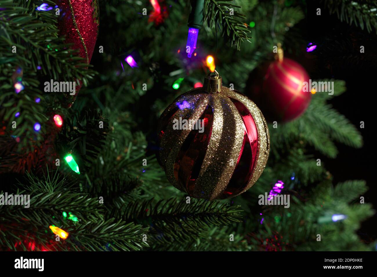 close-up of red and gold sparkly christmas tree decorations hung from a christmas tree with tree lights and bokeh effect lights Stock Photo