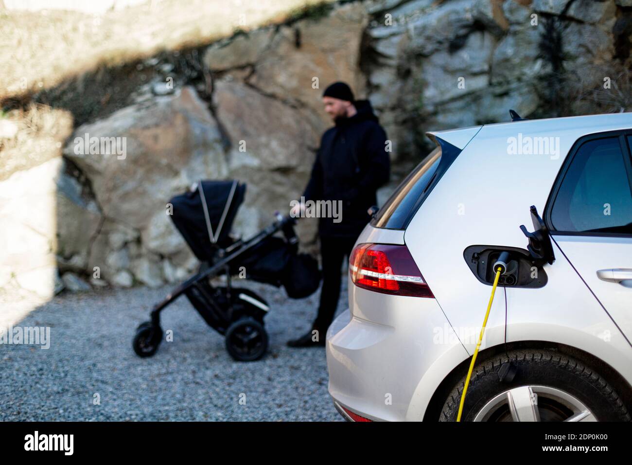 Electric car on charge, man with pram on background Stock Photo