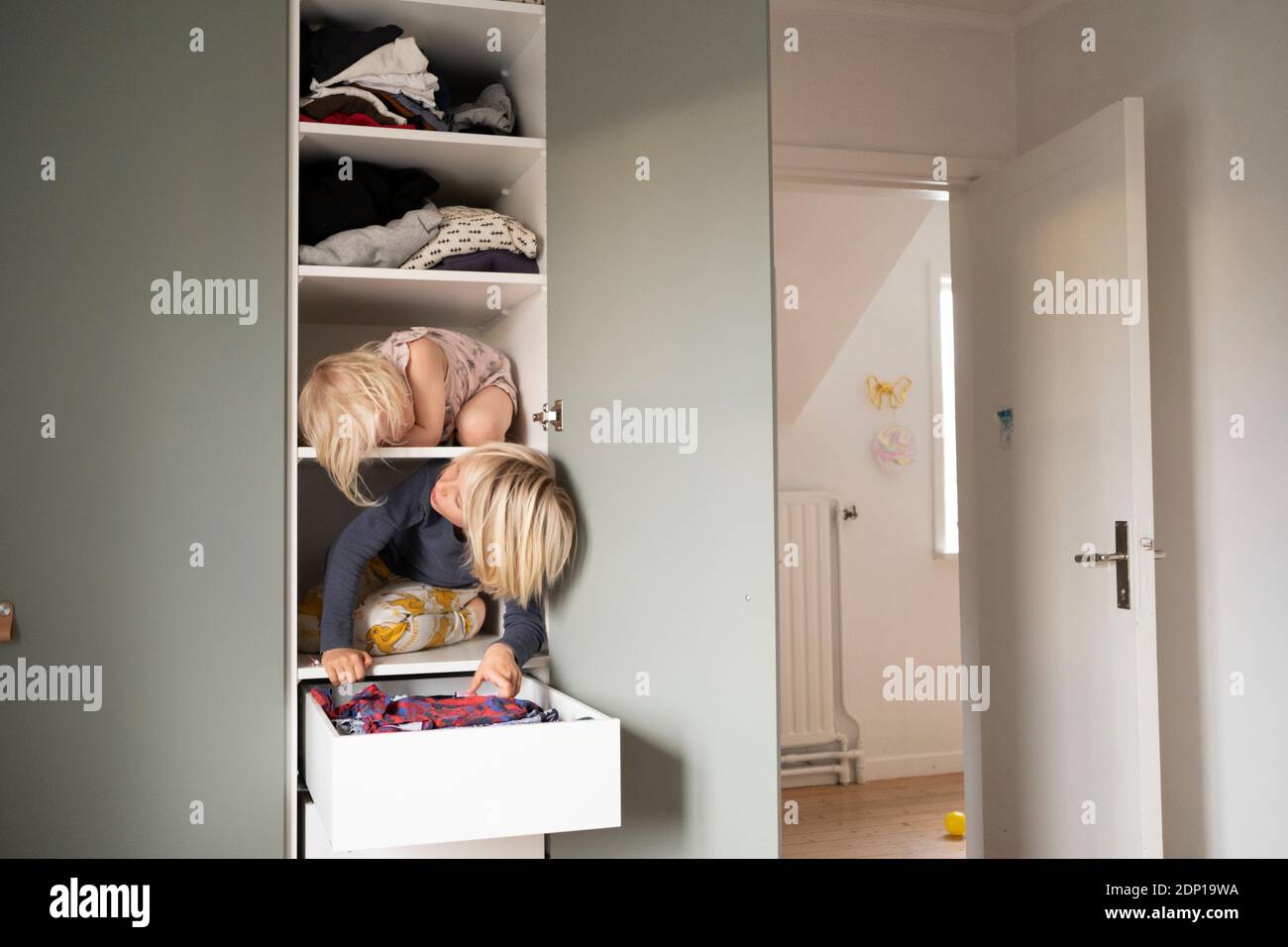 Sisters sitting on shelves in wardrobe Stock Photo