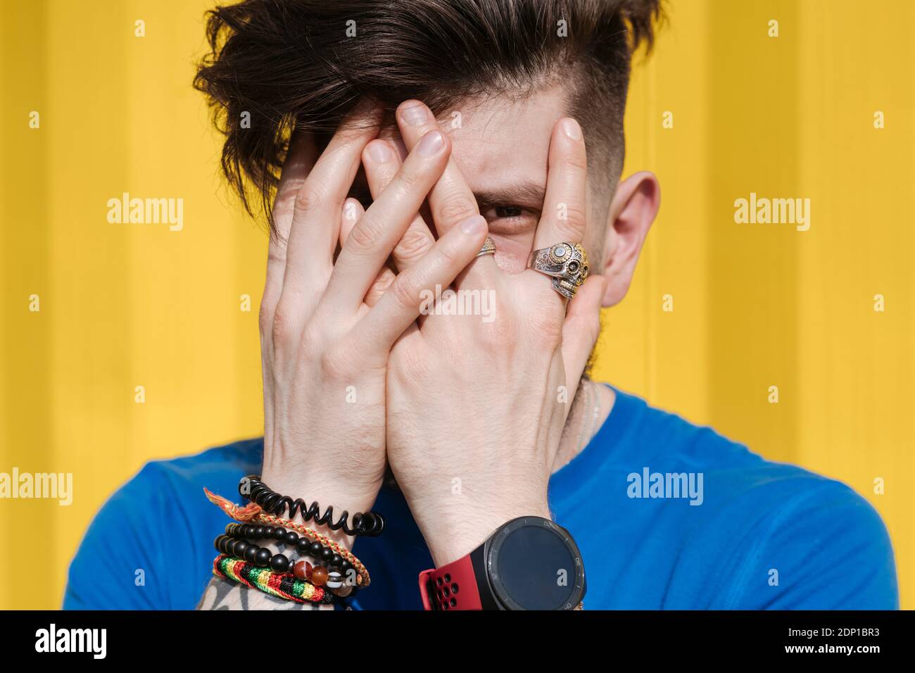 Young man standing in front of yellow wall, hiding face behind his hands Stock Photo
