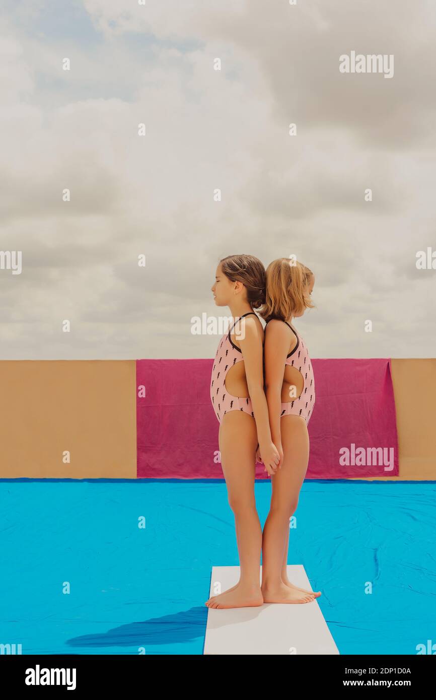 Two girls wearing swimsuits standing back to back with eyes closed outdoors Stock Photo