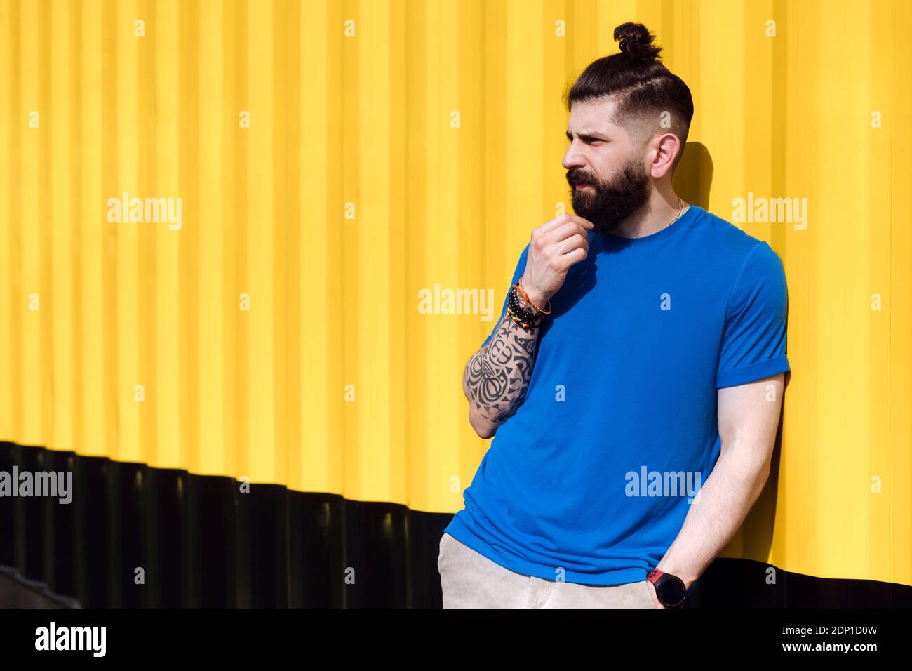 Young man with tattoo leaning on yellow wall Stock Photo
