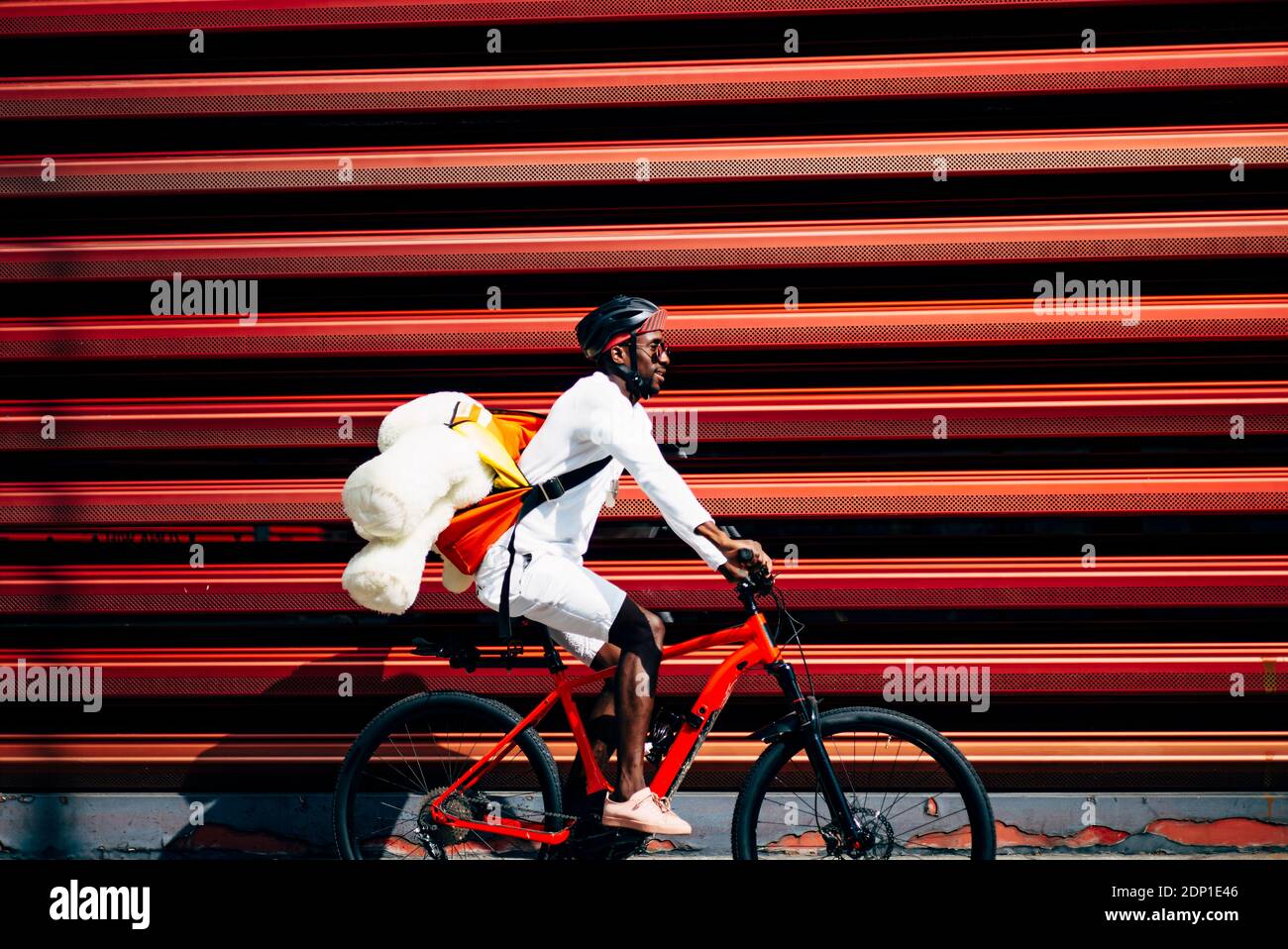 Bicycle courier delivering a teddy bear passing a red wall Stock Photo